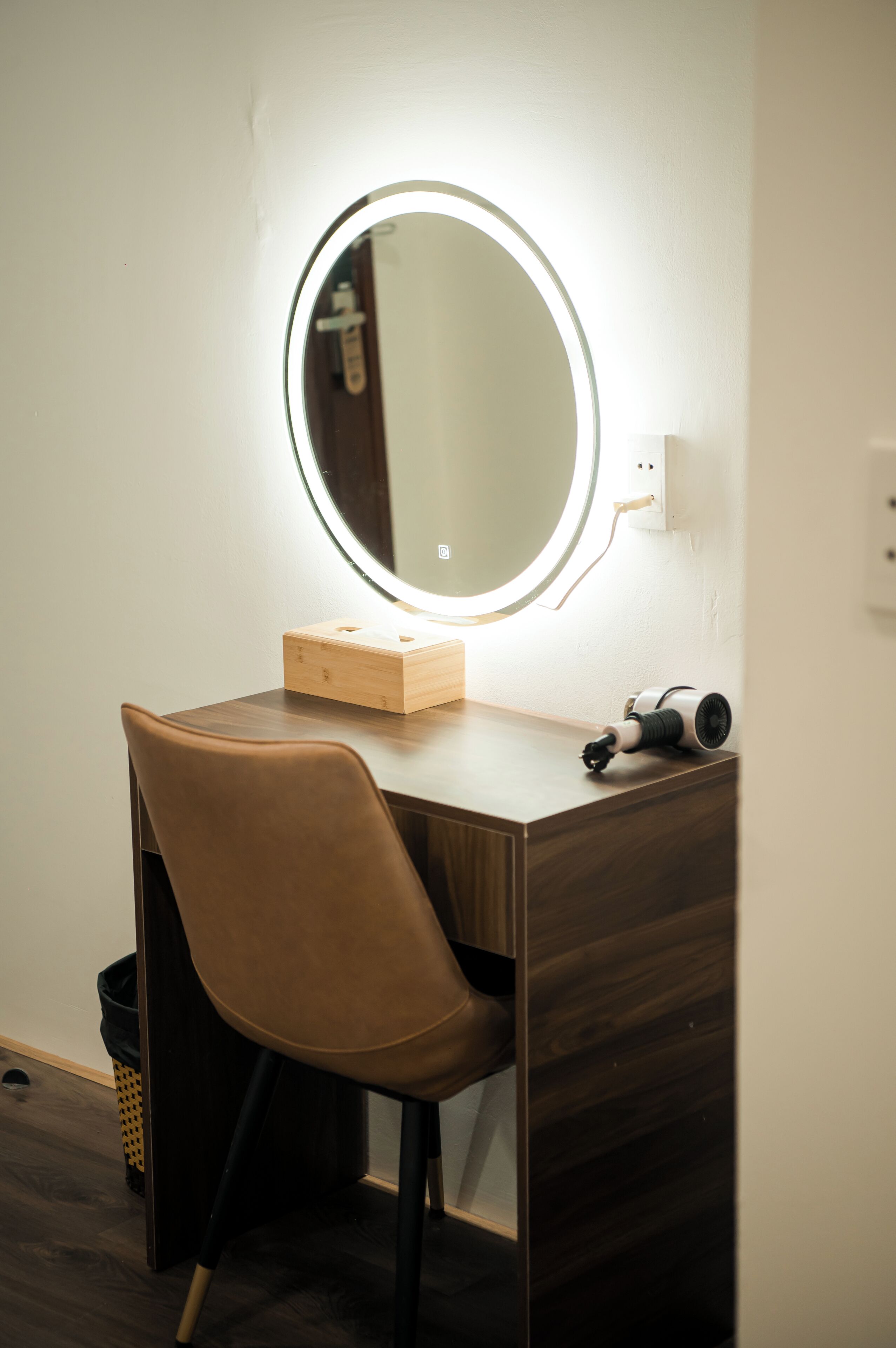 A wooden desk with a round mirror and a hairdryer.