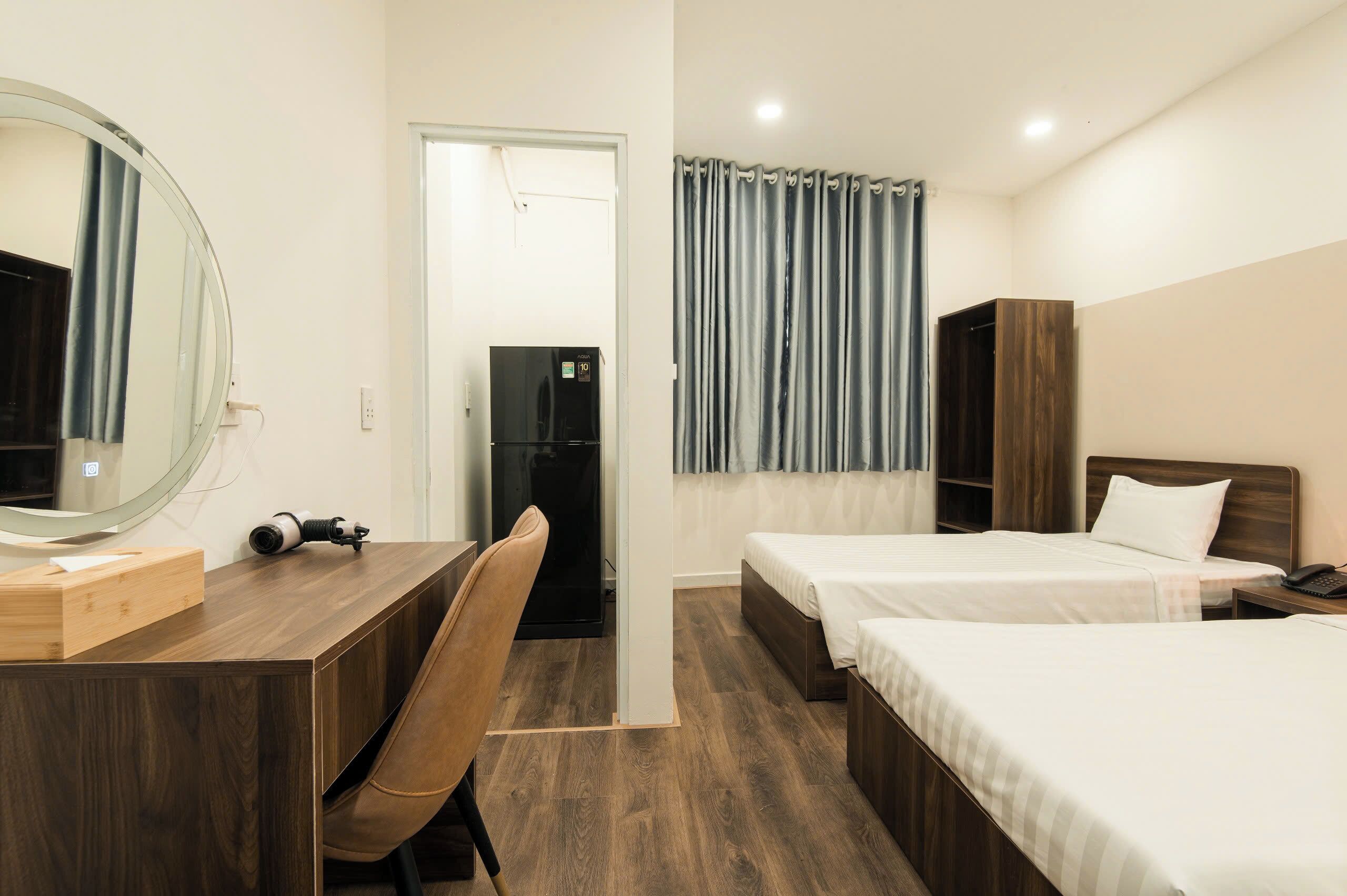 Une chambre d’hôtel avec deux lits, un bureau avec une chaise, un miroir, une armoire et une porte donnant sur une autre pièce.