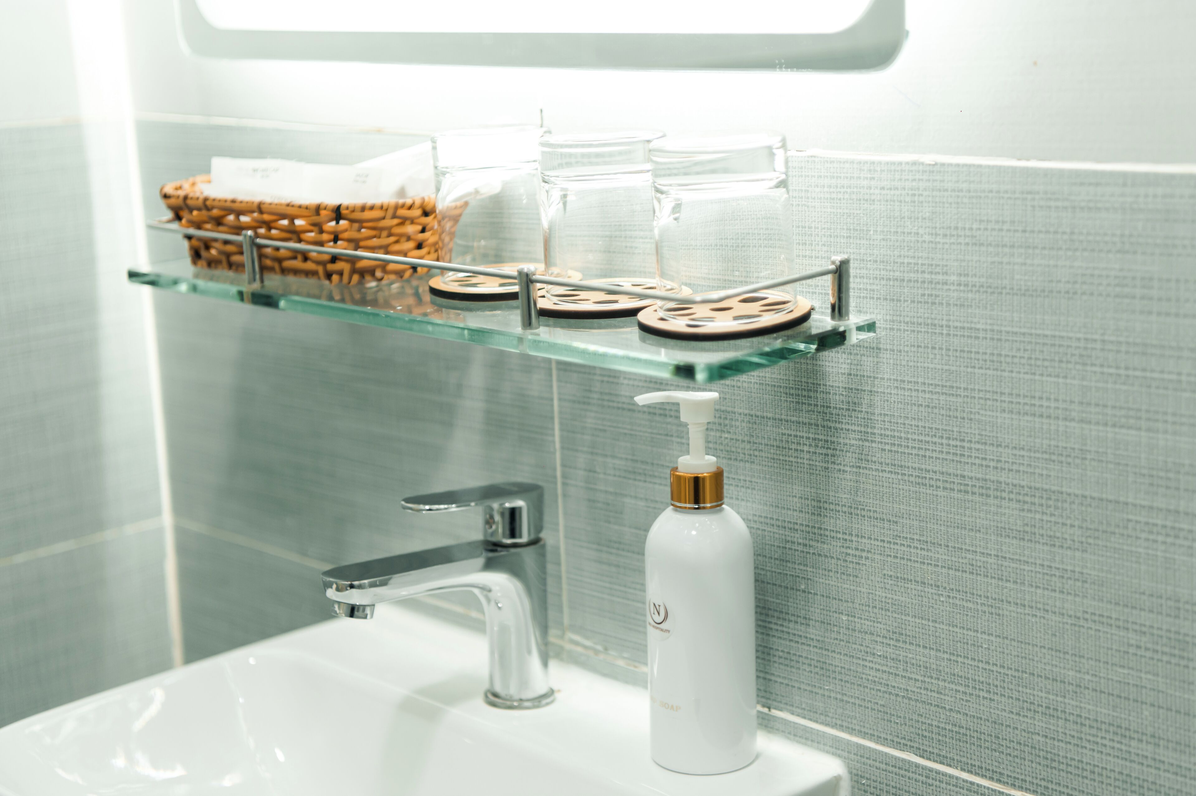 Een badkamer met een glazen plank waarop een mand, potten en een zeepdispenser staan.
