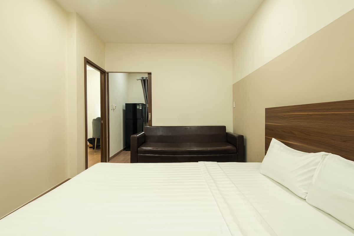 A hotel room with a bed, a brown leather sofa, and a wooden headboard.