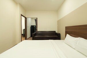 A hotel room with a bed, a brown leather sofa, and a wooden headboard.