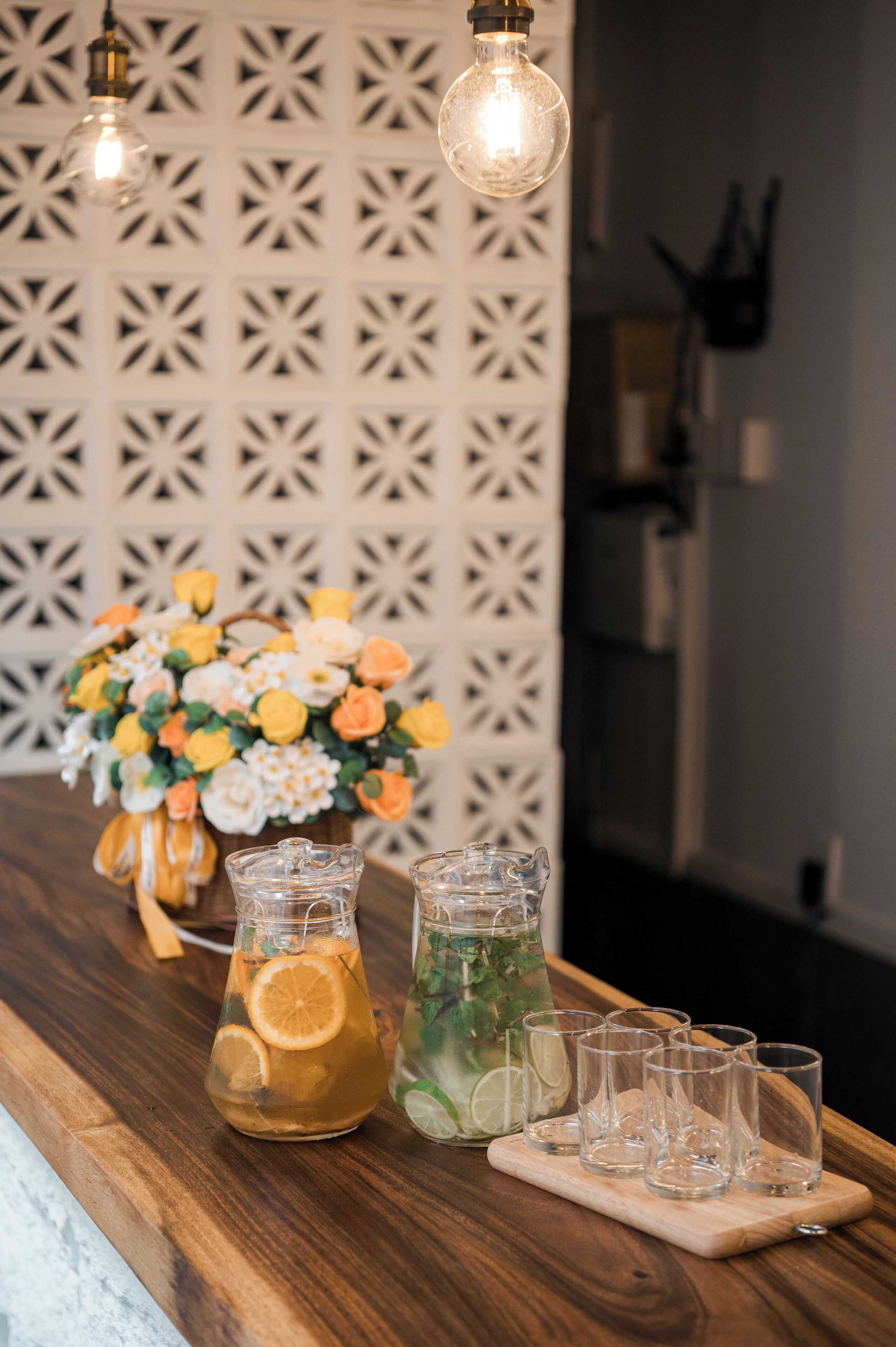 Una barra de madera con dos jarras de bebidas, un florero y lámparas colgantes.