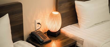 Una camera d'albergo con due letti, un comodino con una lampada e un telefono.