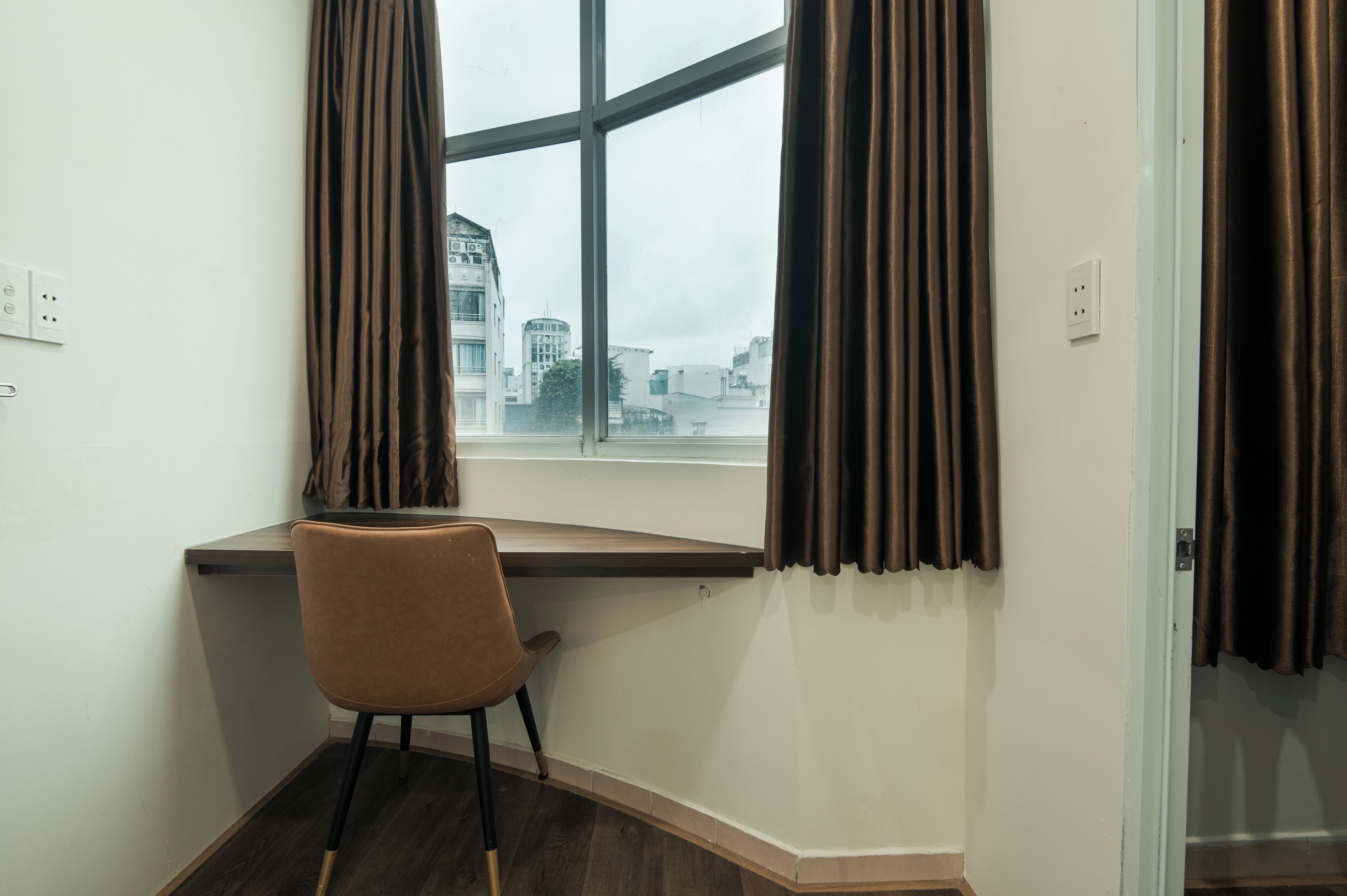 A corner room with a desk, chair, and a large window with curtains.
