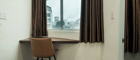 A corner room with a desk, chair, and a large window with curtains.