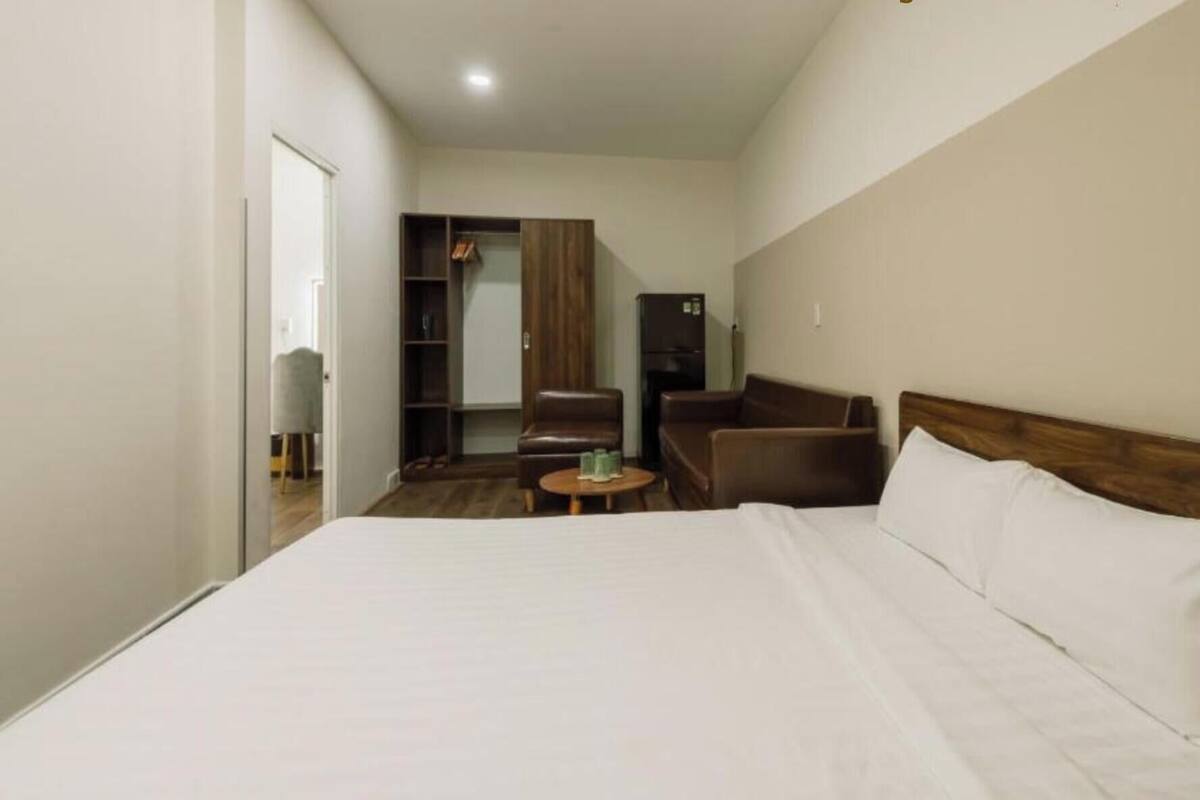 A hotel room with a large bed, a wooden headboard, a seating area with a chair and a small table, and a wardrobe.