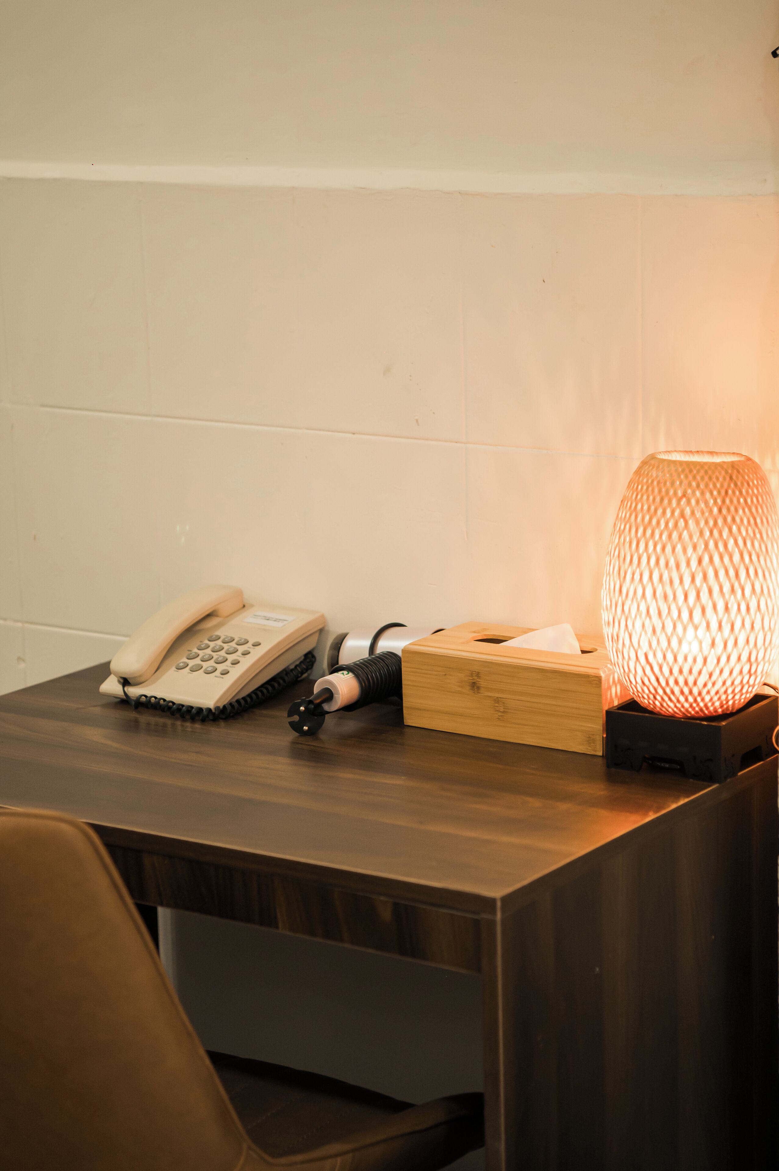 A wooden desk with a telephone, a tissue box, and a lamp.