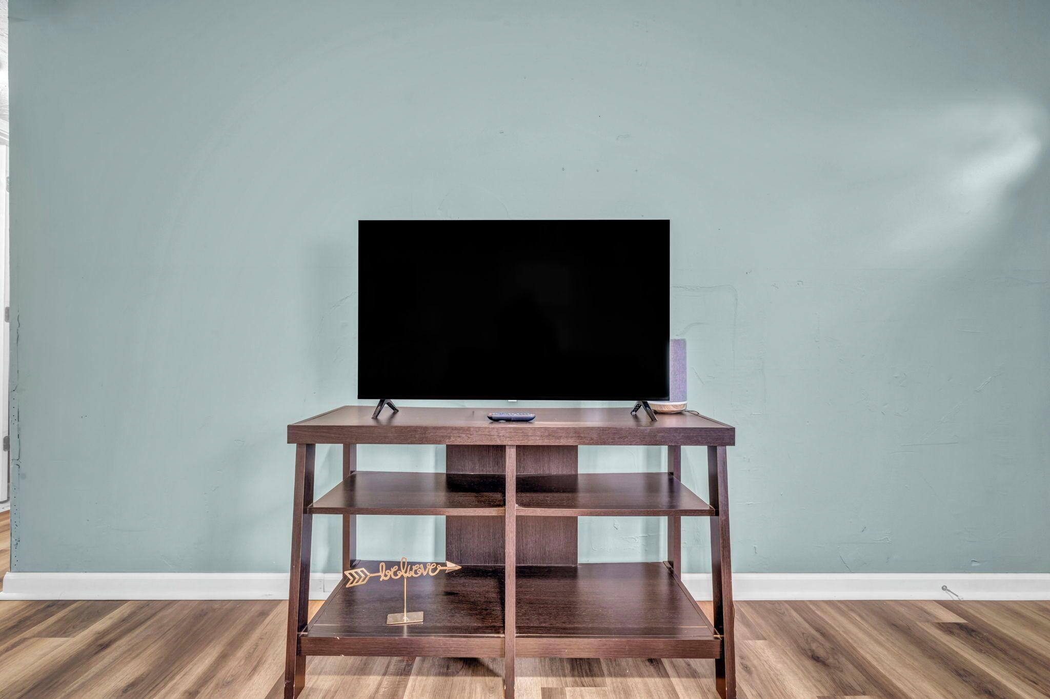 Un meuble en bois pour la télévision, sur lequel est posée une télévision à écran plat, placé contre un mur de couleur turquoise.