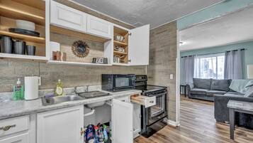 A compact kitchen with white cabinets, a microwave, and an oven. There is a dining area with a gray sofa and a small table.