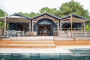 Un espace piscine extérieur moderne, agrémenté d’un escalier en bois menant à un patio couvert avec des sièges d’extérieur.