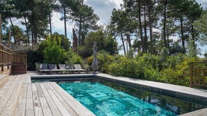 Una terraza de madera con piscina, sillas de descanso y una estatua.