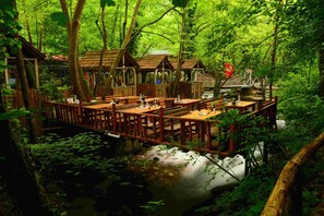 A wooden deck with tables and benches overlooking a river, surrounded by dense forest. - Karaaslan Kamping Tesisleri (Basiskele)