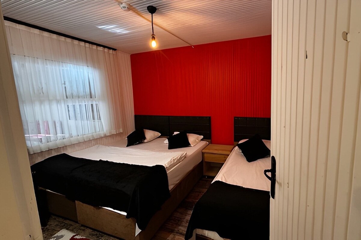 Habitación de hotel con dos camas, una pared de acento roja, cortinas blancas y piso de madera.