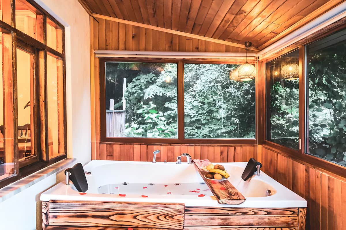Ein Badezimmer einer Holzhütte mit einem großen Fenster, einer Badewanne und einem Holztablett mit Früchten.
