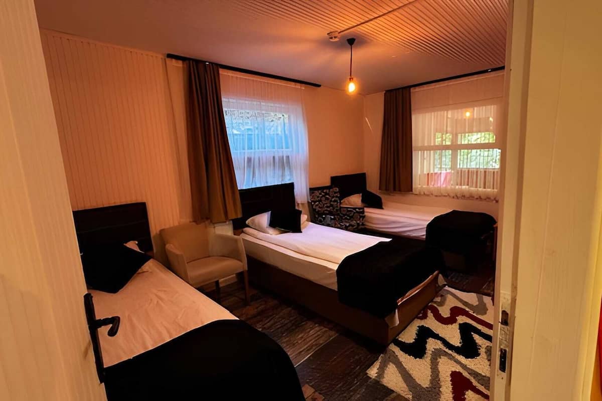 Ein Hotelzimmer mit zwei Betten, einem Sessel, einem kleinen Tisch und einem Fenster mit Vorhängen.