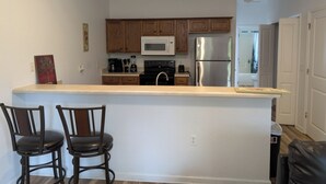 A kitchen with wooden cabinets, a stainless steel refrigerator, a microwave, and a coffee maker. There are two chairs at the counter.