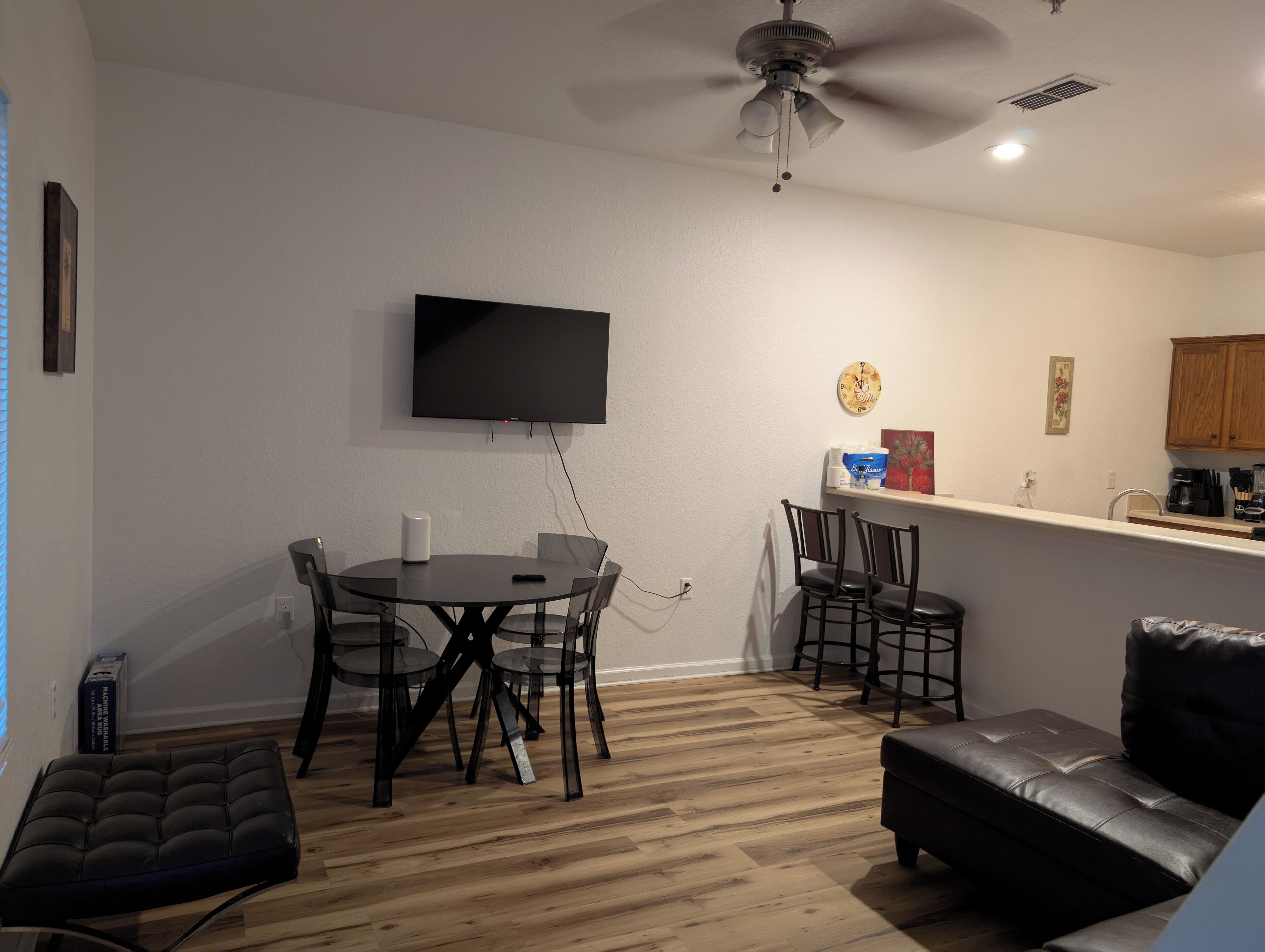A modern living room with a dining area, a ceiling fan, a flat-screen TV, and a kitchen counter.