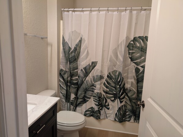 Une salle de bain équipée de toilettes, d’un lavabo et d’un rideau de douche orné d’un motif de feuilles.