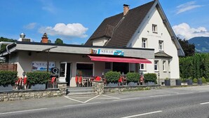 A two-story building with a red awning and outdoor seating. - Gasthaus Sofram (Frastanz)