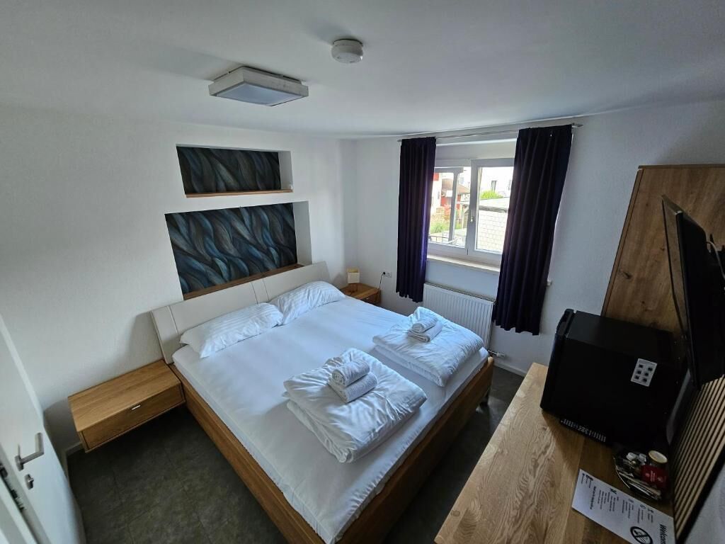 Habitación de hotel con cama doble, mesita de noche de madera, escritorio con computadora y ventana con cortinas.