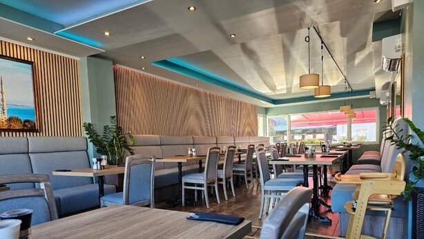 A modern restaurant with high tables and booths, wooden paneling on the walls, and large windows. - Gasthaus Sofram (Frastanz)