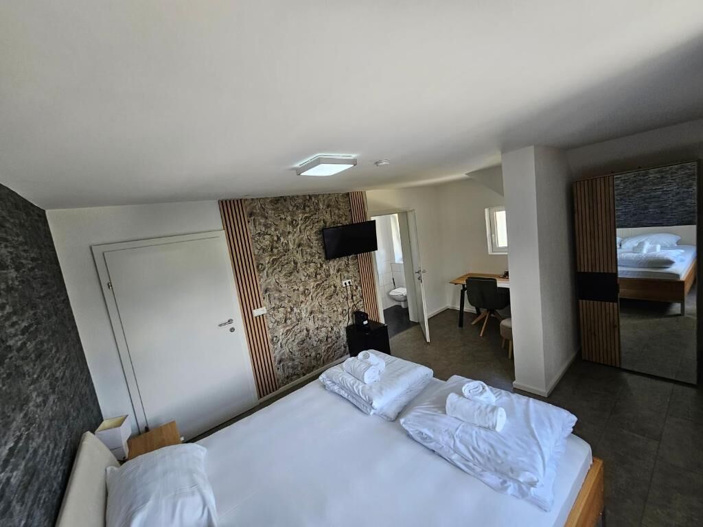A hotel room with a large bed, a desk, a chair, a TV, and a bathroom visible through an open door.
