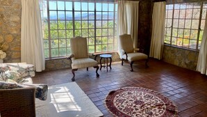A room with stone walls, large windows, two armchairs, a small table, and a patterned rug. - Victorian style cottage in Nyanga - 2096 (Nyanga)