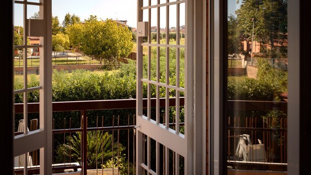 A view from a balcony with a metal railing, overlooking a park with trees and a building in the background. - Hibiscus Apartment (Ciampino/Rome/Roma) (Ciampino)