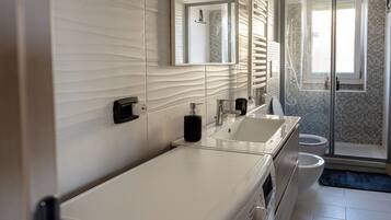 A modern bathroom with a large mirror, two sinks, a shower, and a toilet.