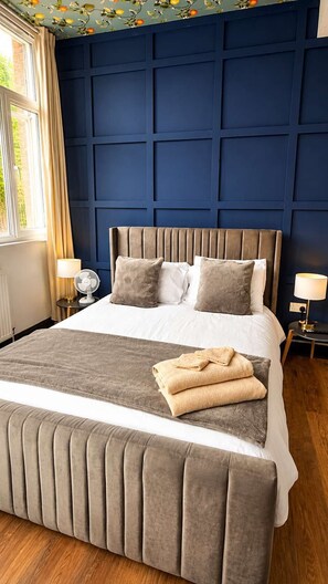 A bedroom with a large bed, a headboard, two bedside tables, and a window with curtains.