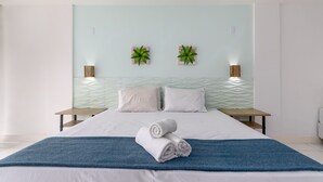 Ein modernes Hotelzimmer mit einem großen Bett, zwei Nachttischen, einer blauen Tagesdecke und zwei Wandpflanzen.