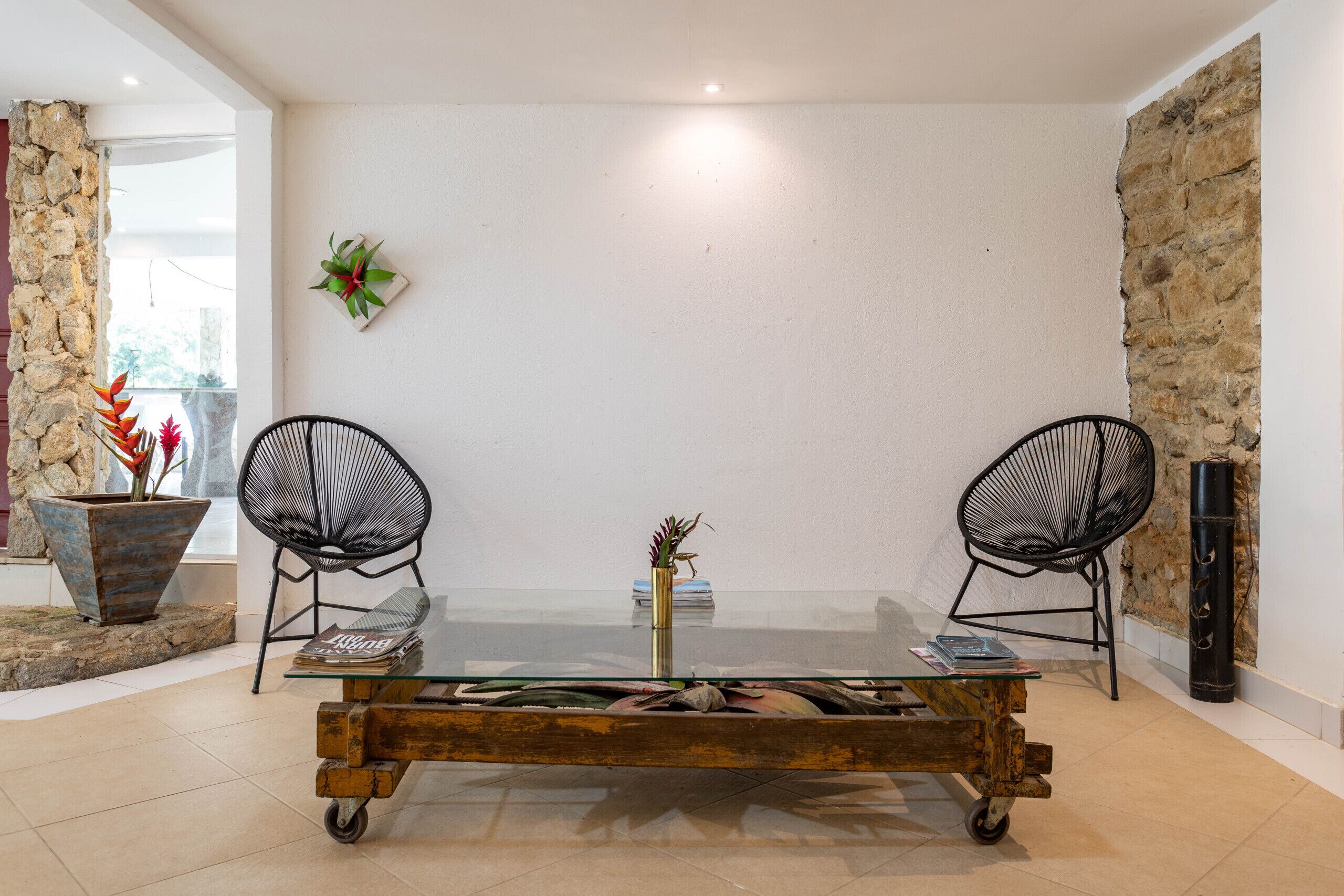 A dining area with a glass table, two black chairs, a vase with flowers, and a stone wall.