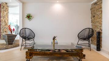 A dining area with a glass table, two black chairs, a vase with flowers, and a stone wall.