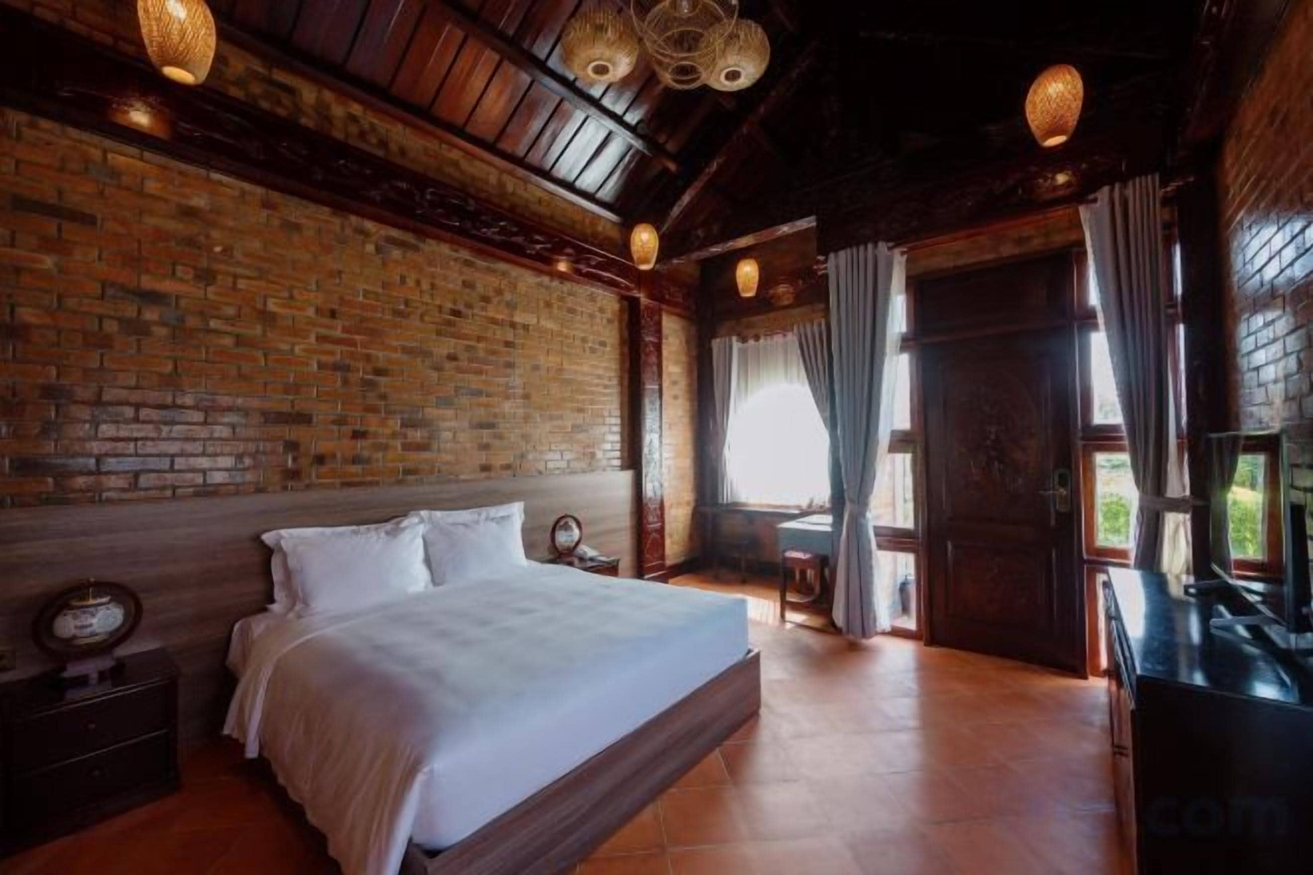 Un dormitorio con pared de ladrillo, cama de madera, mesita de noche y ventana con cortinas.