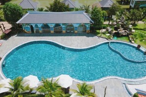A swimming pool with a curved design, surrounded by palm trees and a covered pavilion. - Cantho Eco Resort (Can Tho)