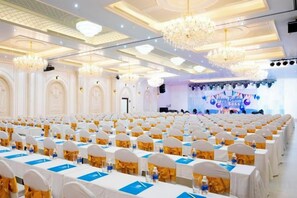 A banquet hall with rows of tables, chandeliers, and a stage with a blue backdrop. - Cantho Eco Resort (Can Tho)