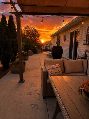Une terrasse couverte avec un banc en bois et des coussins, des guirlandes lumineuses et une vue sur le coucher du soleil.