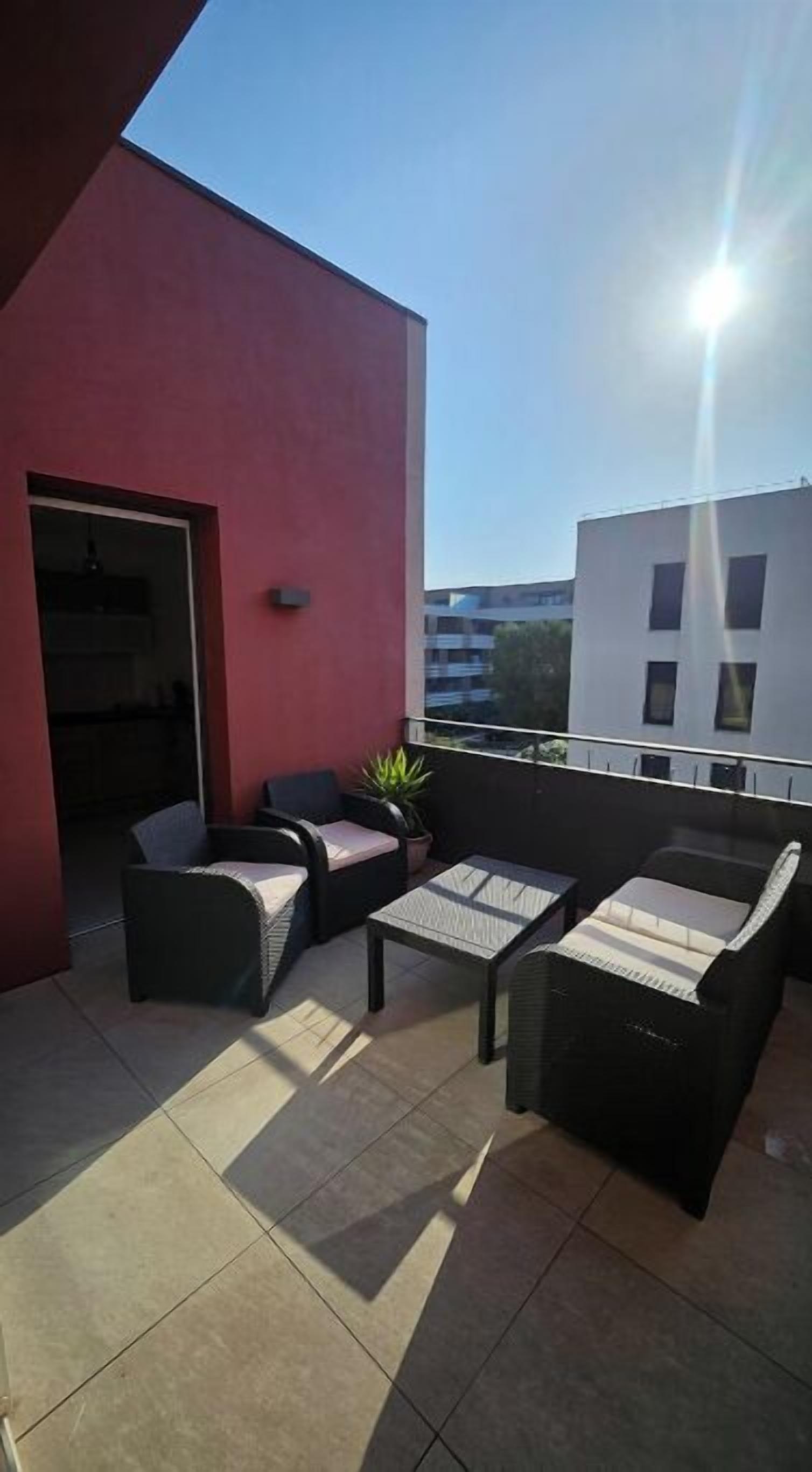 Eine Dachterrasse mit Gartenmöbeln, einem Topf mit Pflanze und Blick auf ein modernes Gebäude.