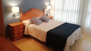 A hotel room with a wooden bed, two bedside tables, a nightstand, and a window with curtains. - Pension San Vicente (San Vicente de la Sonsierra)