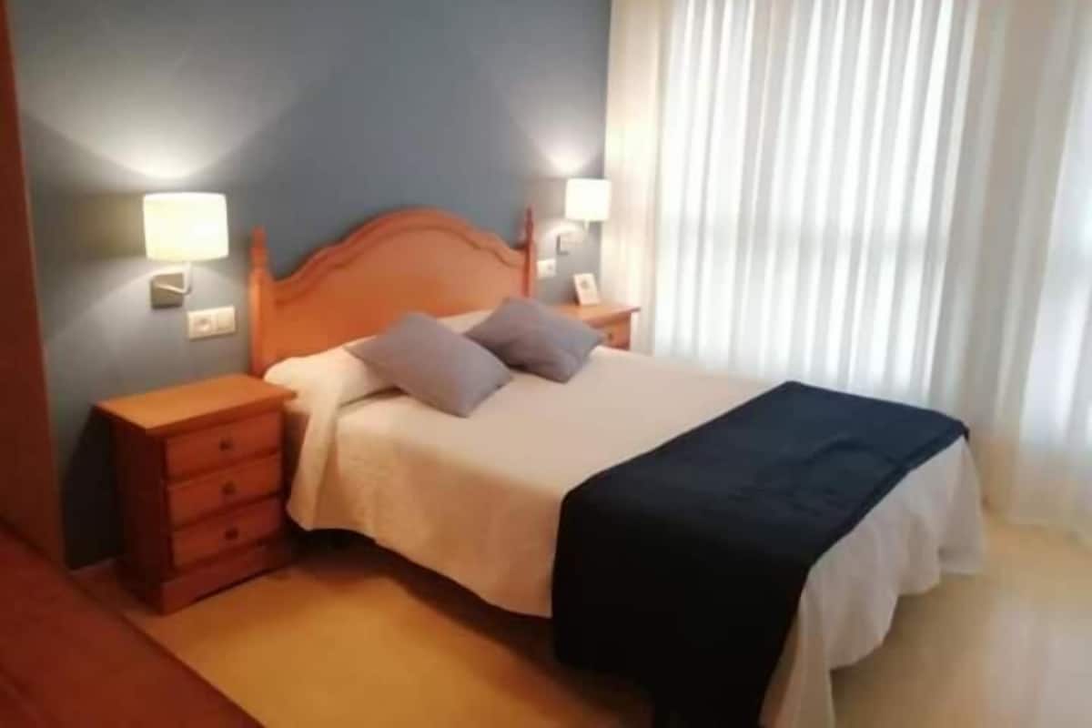 Ein Hotelzimmer mit einem Holzbett, zwei Nachttischen, einem Fenster mit Vorhängen.