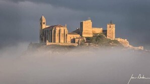 A historic building with a bell tower, a large central tower, and a smaller tower, surrounded by mist. - Pension San Vicente (San Vicente de la Sonsierra)