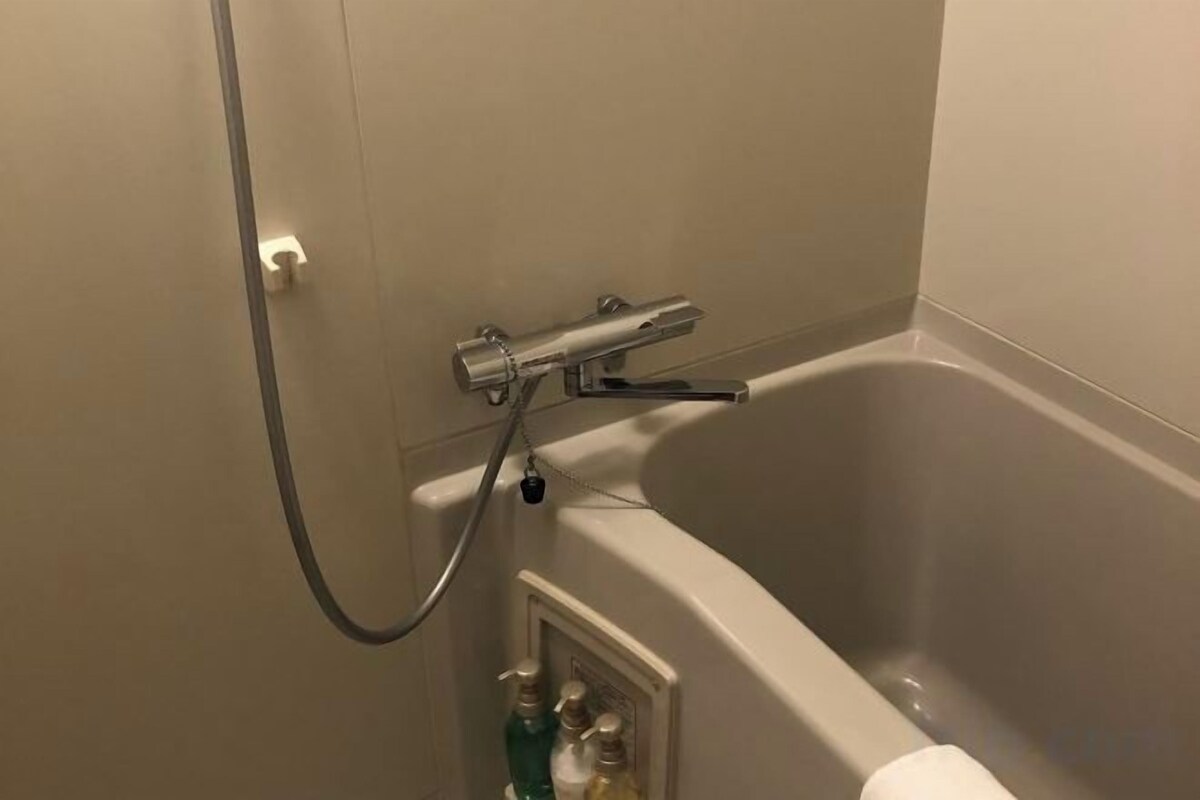 A bathtub with a handheld showerhead, a towel rack, and a bottle of shampoo.
