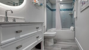 Casa de banho moderna com toucador branco, espelho redondo, sanita e banheira.