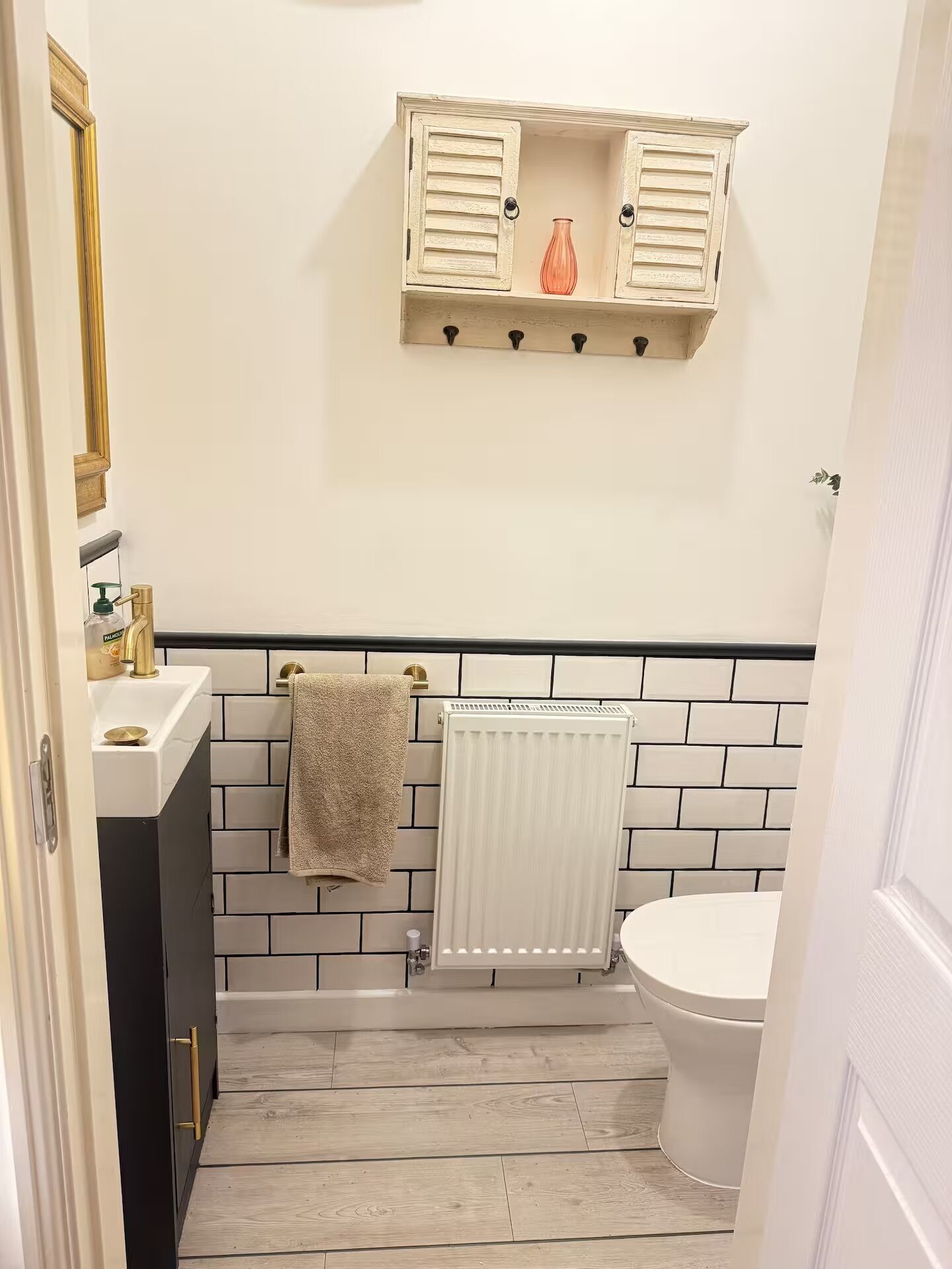 Un bagno con un lavandino bianco, un mobile contenitore nero, un asciugamano appeso al muro, un water bianco e un termosifone.