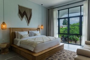 Slaapkamer met een groot bed, twee bedlampen, een houten hoofdbord en uitzicht op groen buiten, plus een groot raam.