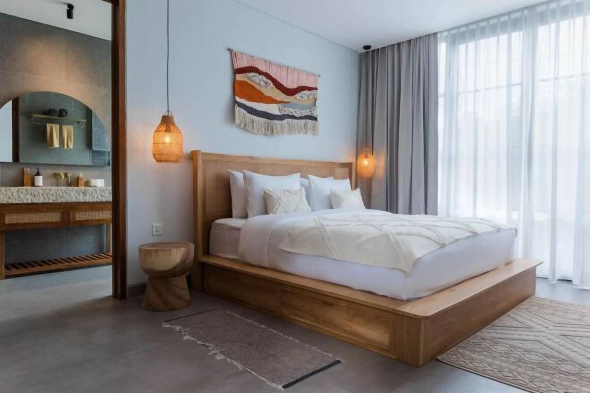 Een moderne slaapkamer met een houten bed, een ingebouwde bank, een grote spiegel en een decoratief wandkunstwerk.