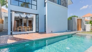 Een modern huis met een zwembad, een terras met tuinmeubilair en een groot raam met uitzicht op het zwembad.