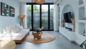 Een moderne woonkamer met een bank, een ronde houten salontafel en een aan de muur bevestigde televisie.