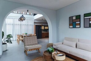 Ein modernes Wohnzimmer mit einer Couch, einem Sessel und einem Couchtisch, einem Bogen zur Essecke und abstrakter Wandkunst.