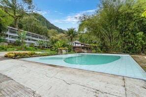 Ein Poolbereich mit gefliestem Deck, umgeben von üppiger Vegetation und einer Bergkulisse.